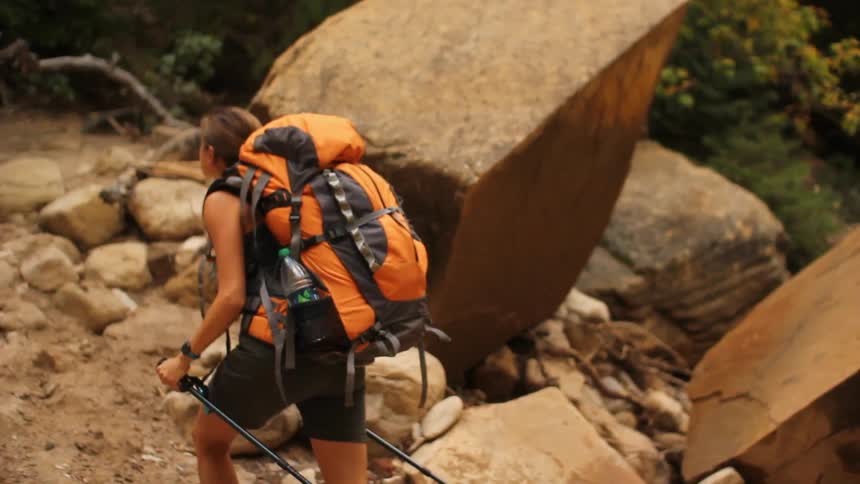 A woman wearing a backpack hikes up a rocky trail