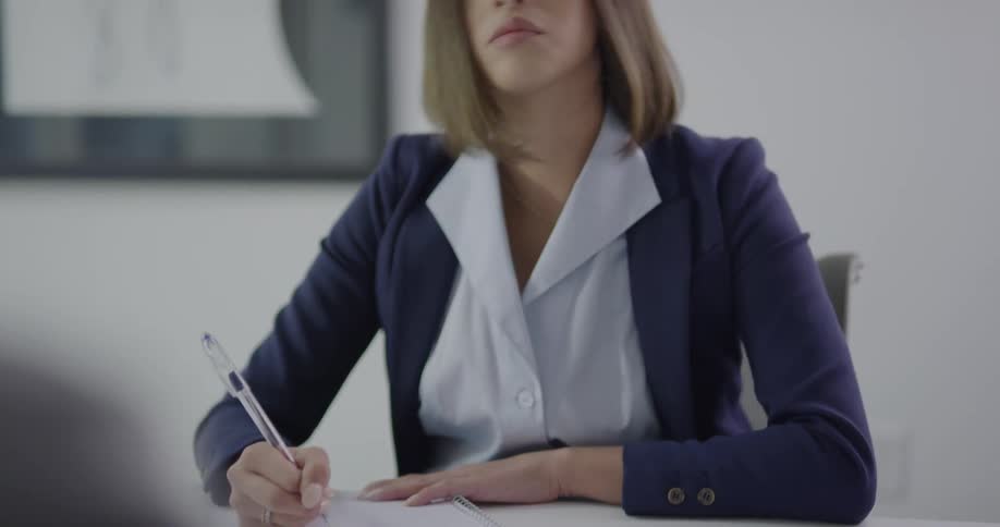A woman sitting at a desk with a pen writing on a pad