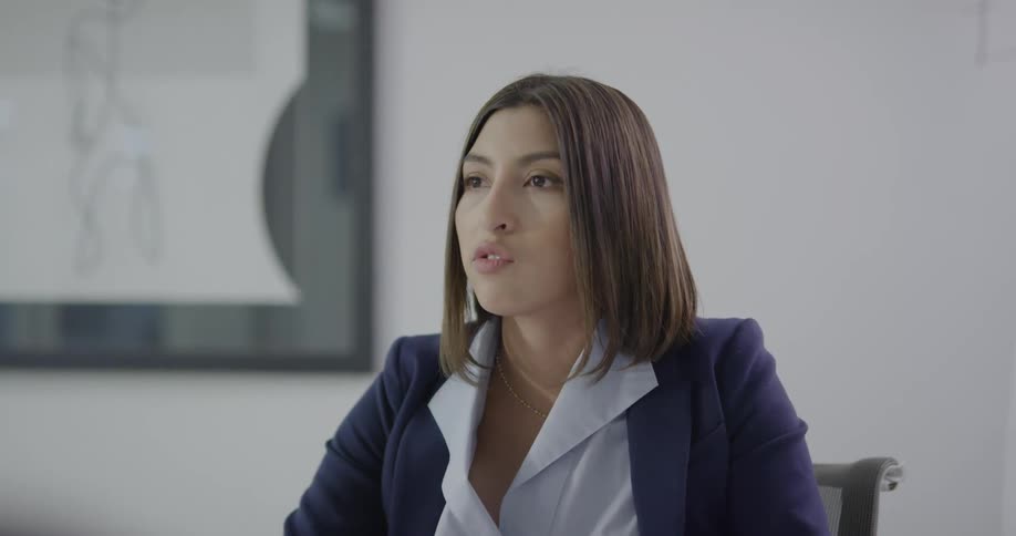 A woman sits in an office and talks with at least one other person