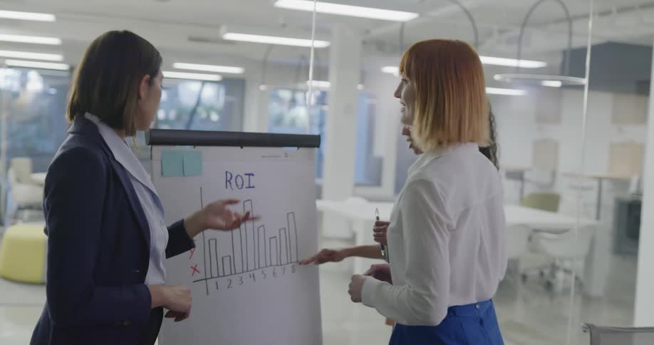 Three women in an office talking and looking at a chart