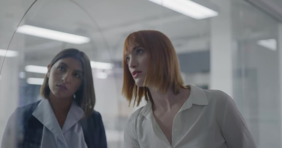 A woman writing on a clear board and talking while two other women listen