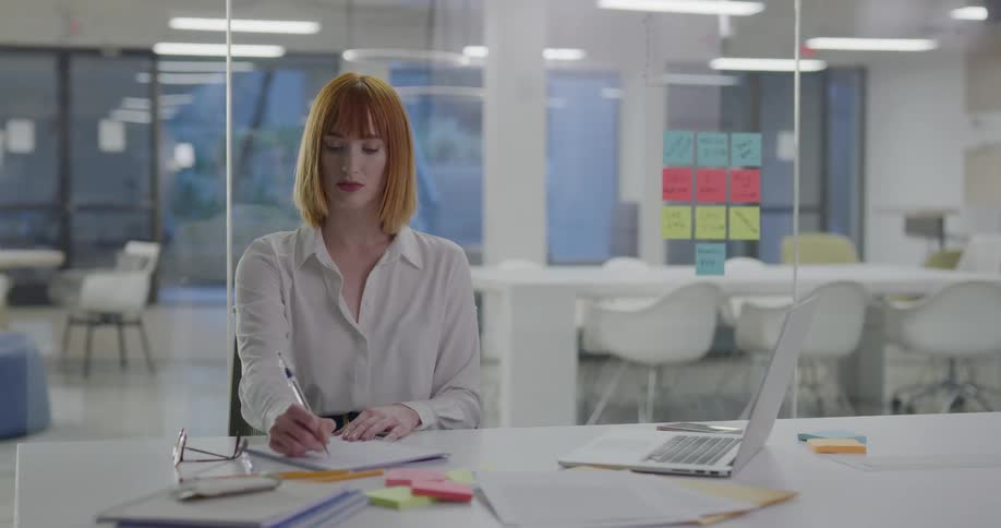 A woman sits in an office and writes in a notebook