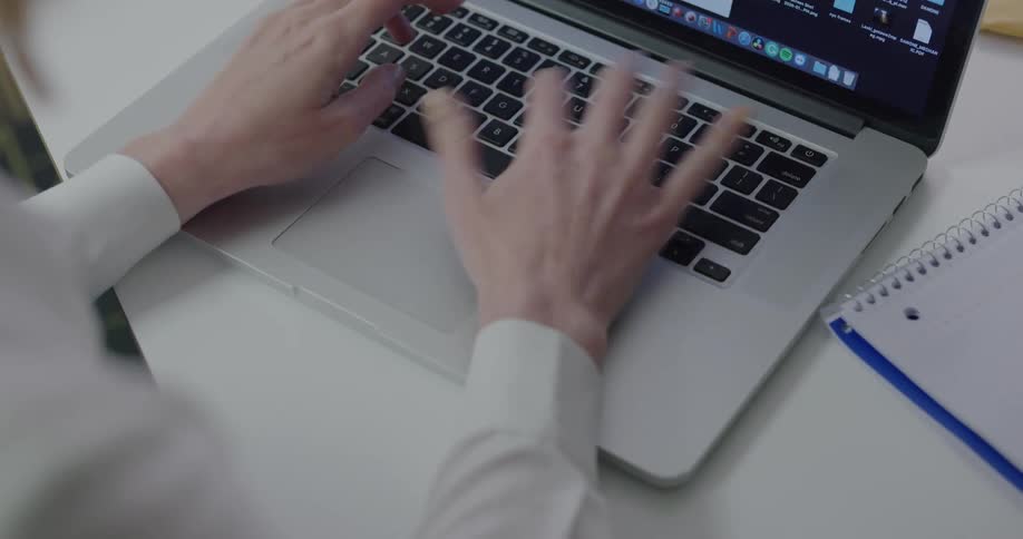 A woman types on her laptop and then writes in a notebook