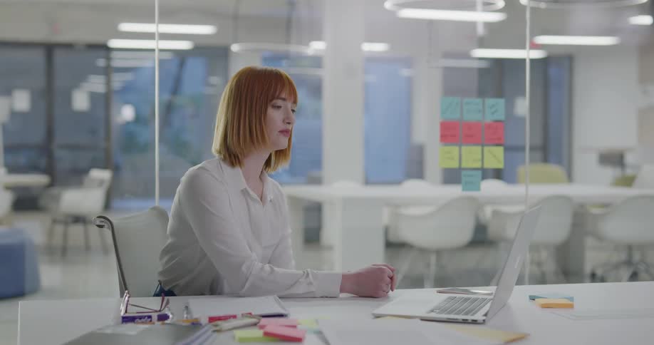 A woman sitting at a desk looking at a laptop