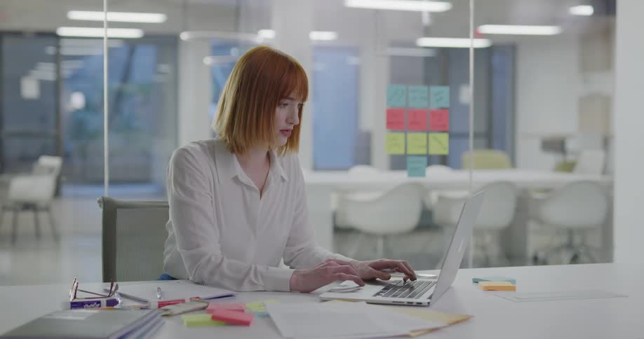 A woman in an office sits at a table and types on a laptop