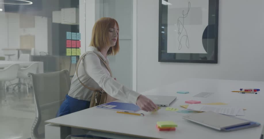 A woman walks in to an office and puts her laptop and supplies down on a desk