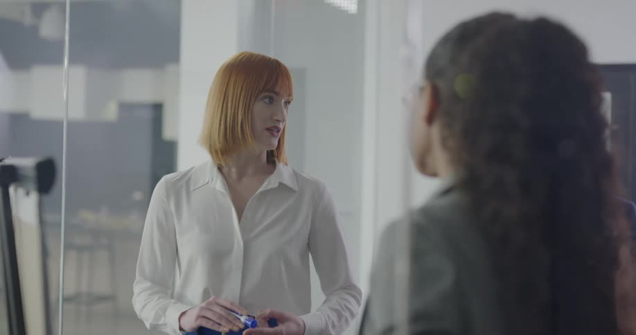 Two women in an office standing and talking with one writing on a pad with a marker