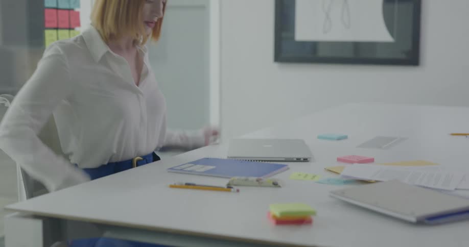 A woman walks in to her office and puts her laptop down sets a notebook out and starts writing
