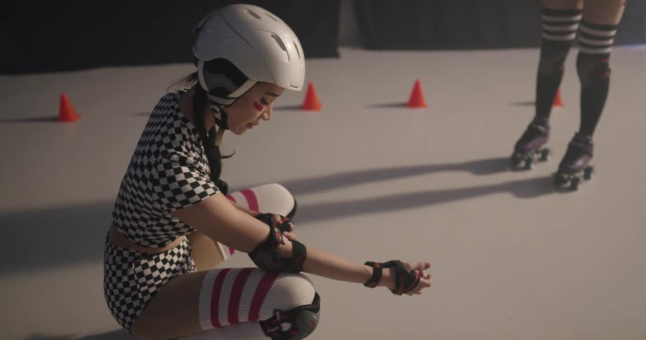 A girl with roller skates and a helmet putting on elbow pads
