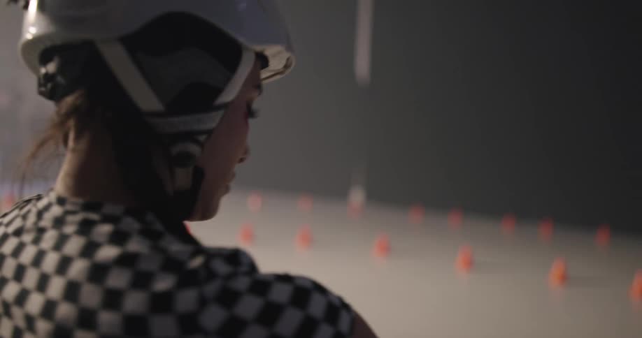 A woman with a helmet on puts on gloves and looks at the rink