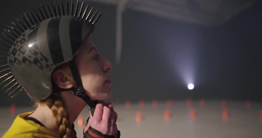 A woman with roller skates sitting on the floor putting on a helmet