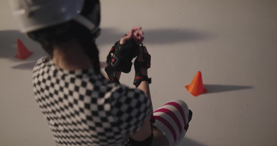 A woman with a helmet and elbow pads putting on gloves