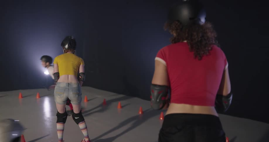 Women with helmets and elbow pads roller skating indoors