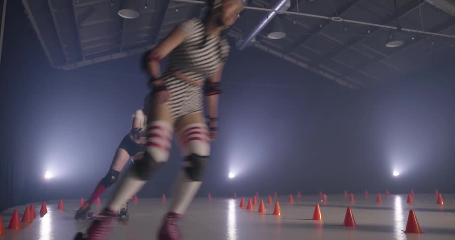 Four women wearing helmets and pads rollerskate around a cone outlined track laughing and racing