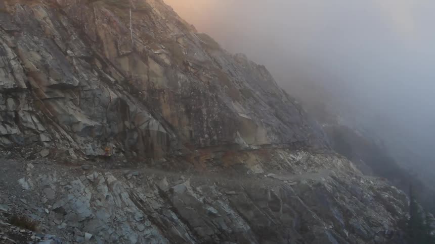 A backpacker walks a narrow path along a cliff edge in the fog