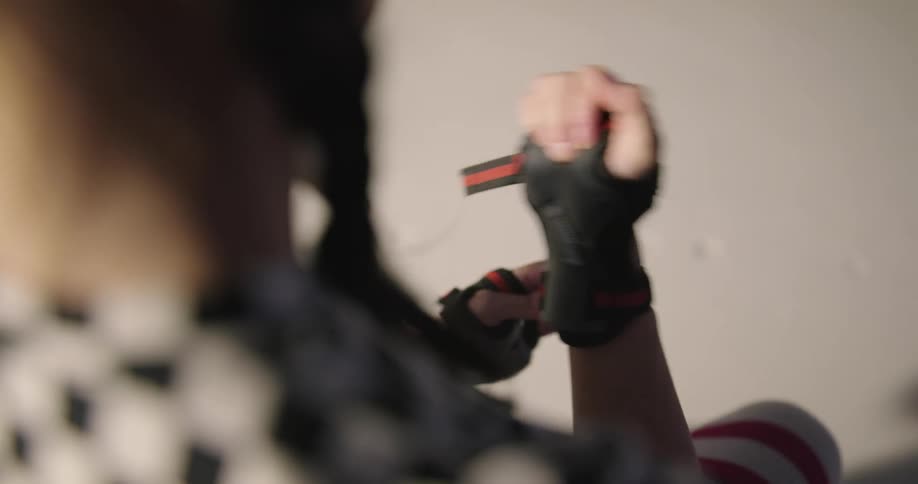 A woman puts on wrist guards to add to knee and elbow pads and helmet before she roller skates off