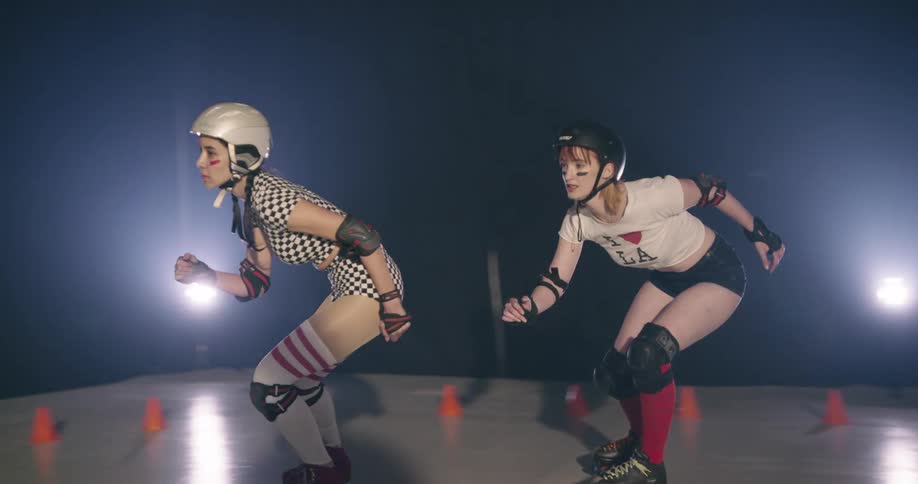 Women roller skate and try to pass each other on a small rink with a track marked by orange cones