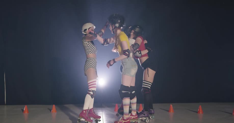 Women roller skaters in shorts and helmets hug and high five at a rink