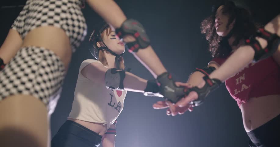Four women stand in a circle and put their hands together and cheer