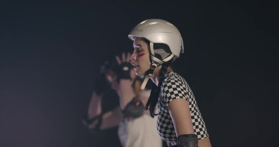 Two women line up in pads and helmets ready to race on rollerblades