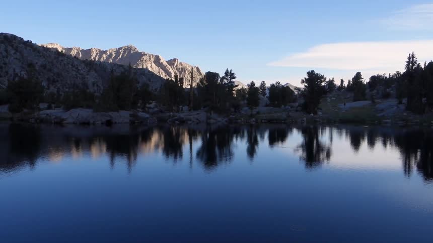 A quiet body of water, that is reflecting the trees and rocks along the shoreline, in a mountainous region