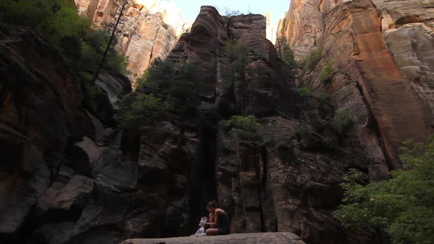 A person is sitting on a rock platform next to the side of a mountain