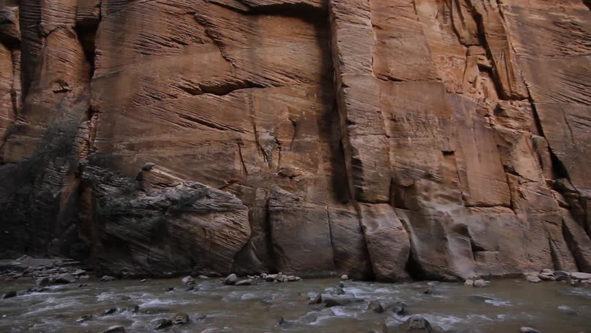 A stream flows by a canyon rock face
