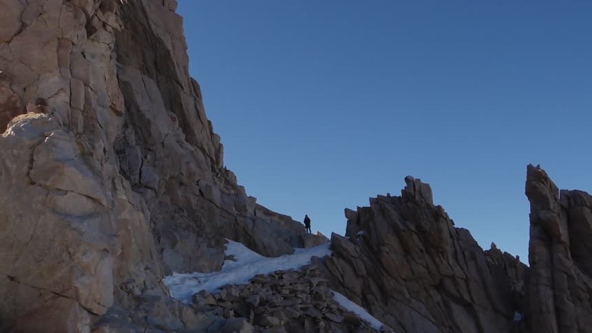 A person standing at the edge of a mountain path looking out at the blue sky
