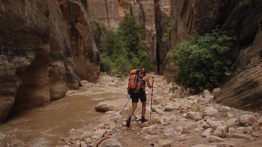 A woman hikes past a rocky stream
