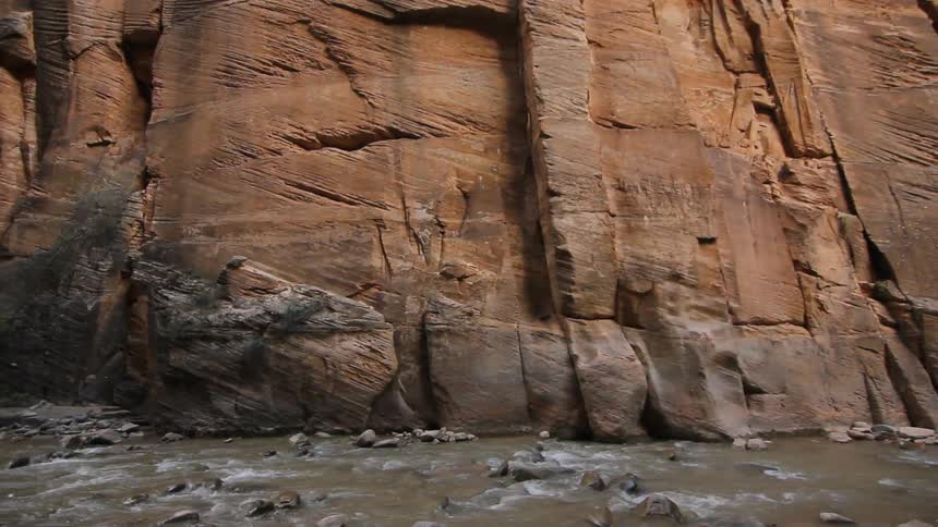 Water flowing around rocks at the foot of a steep, relatively smooth cliff