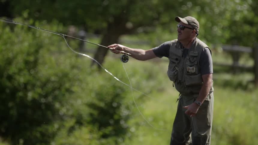 A man in fishing attire casts a line from a fishing pole