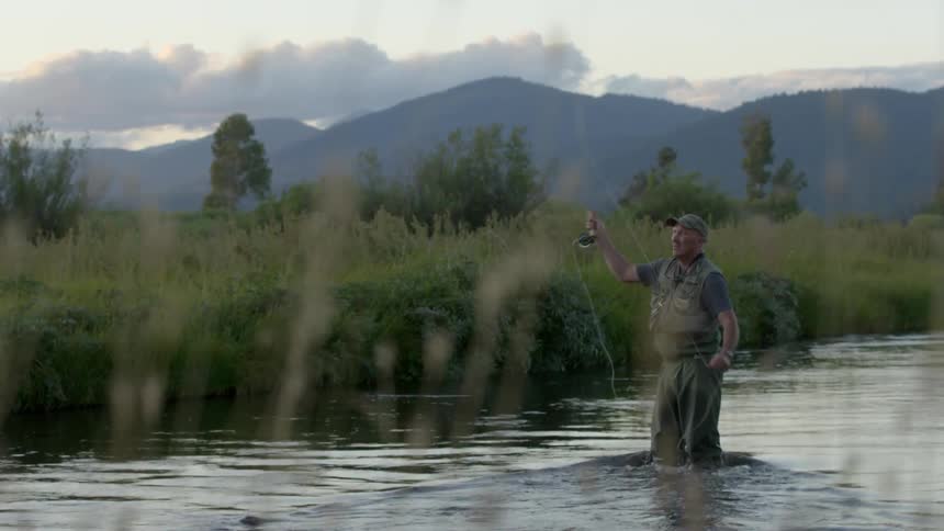 A fisherman casts a line while standing in a river