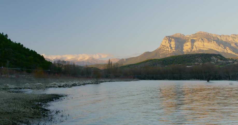Cars travel past a mountain lake with a rippling surface that reflects the sky and ridge on the horizon