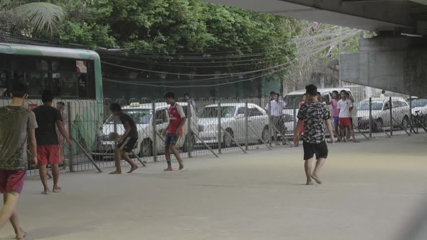 Young men play soccer under bridge next to stalled traffic