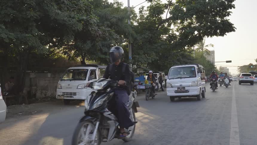 People ride motorcycles on a city street with passengers including young children riding in front