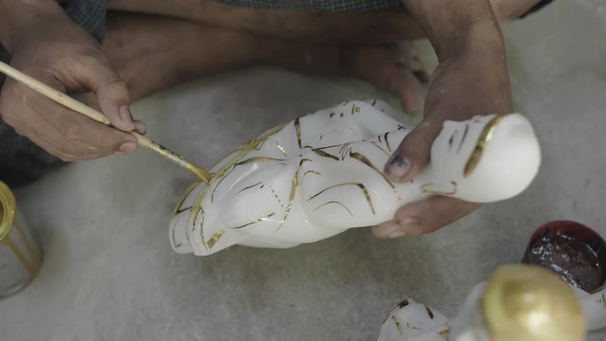 A man sits on the ground and paints a figurine