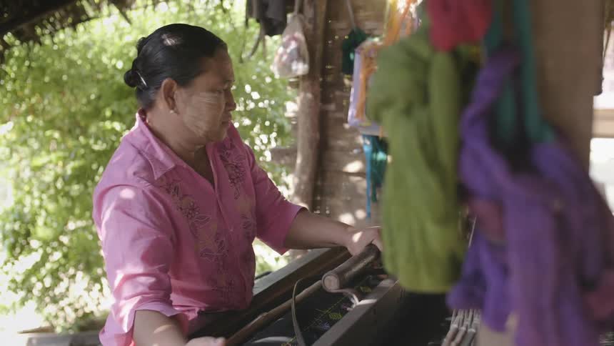 Woman weaves on loom in building with open sides