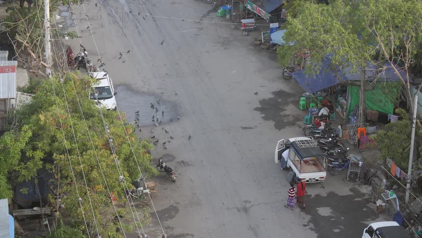 People walk and ride motorbikes down a street in a third world country
