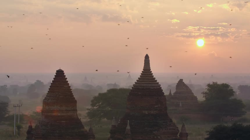 Birds fly over ancient buildings at sunset