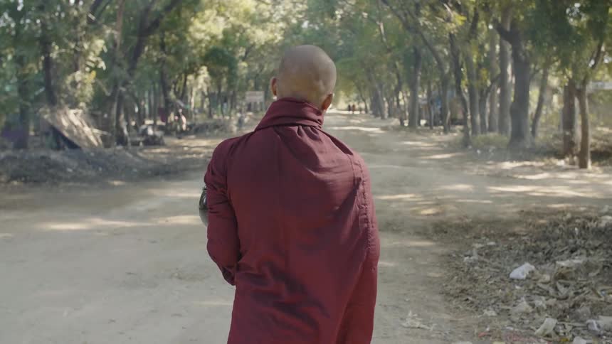 A man in a burgundy robe walking down a dirt path