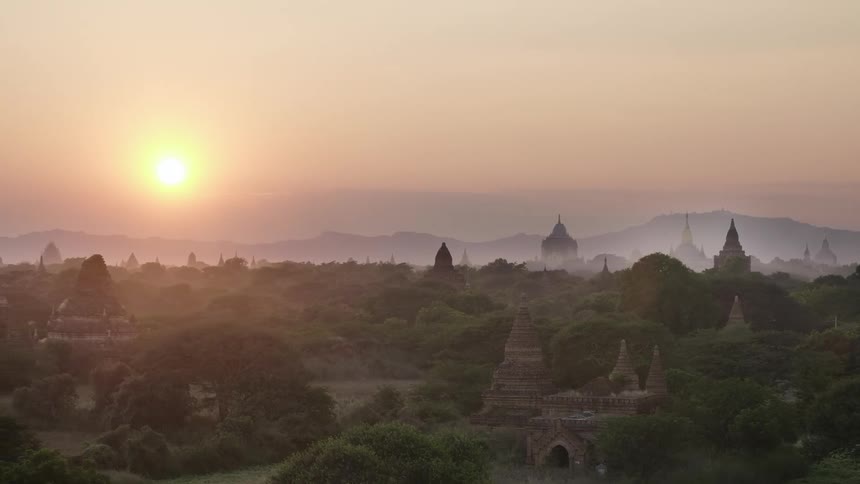 The sun hangs low in the sky over an ancient temple complex in the jungle