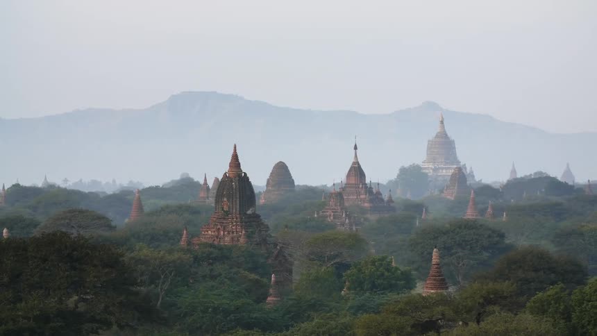 Temple tops stand above the trees with the silhouette of a mountain ridge behind
