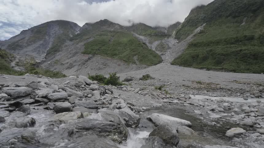 A small stream flows over rocky terrain in front of a mountain range