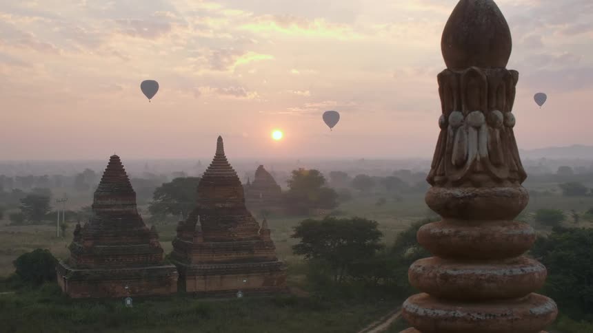 Sun sits just above the horizon as hot air balloons float over pagodas