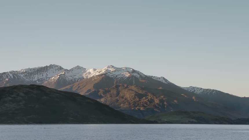 Snow sits on mountains next to a lake
