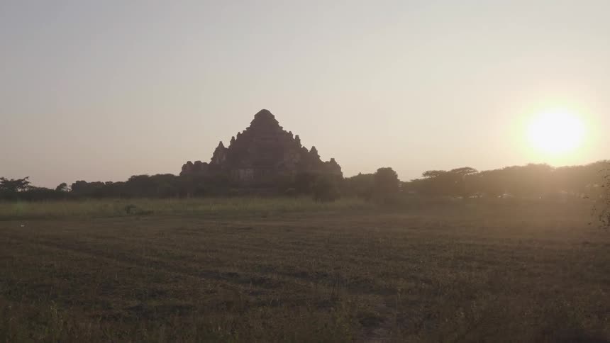 Sun glares on the horizon as pagoda rises in the middle of a plain
