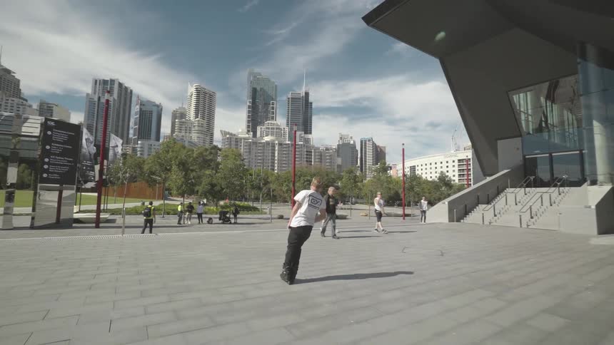 A teen roller skates and performs jumps as other teens walk along