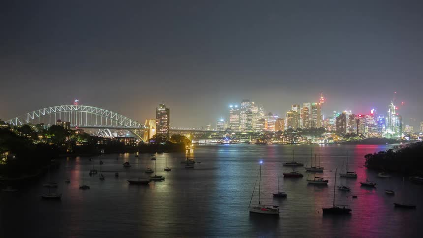 Boats float in a river that runs by a busy city at night