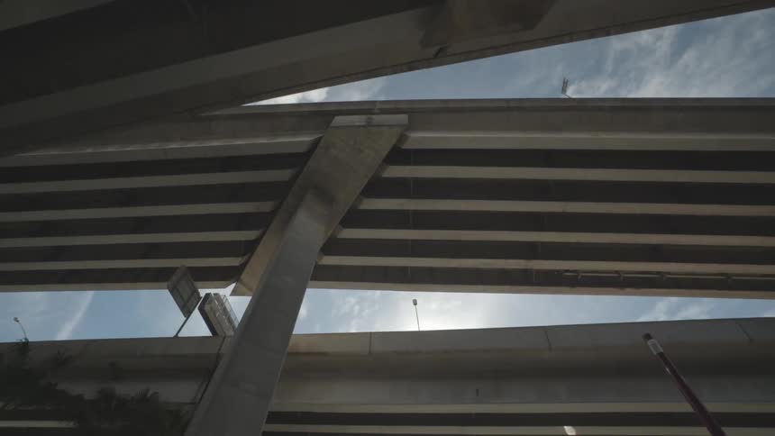 Underneath an overpass with a vehicle driving by with the sky in the background