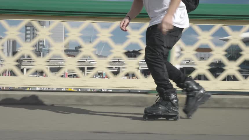 A young adult male rides roller blades on a pedestrian bridge